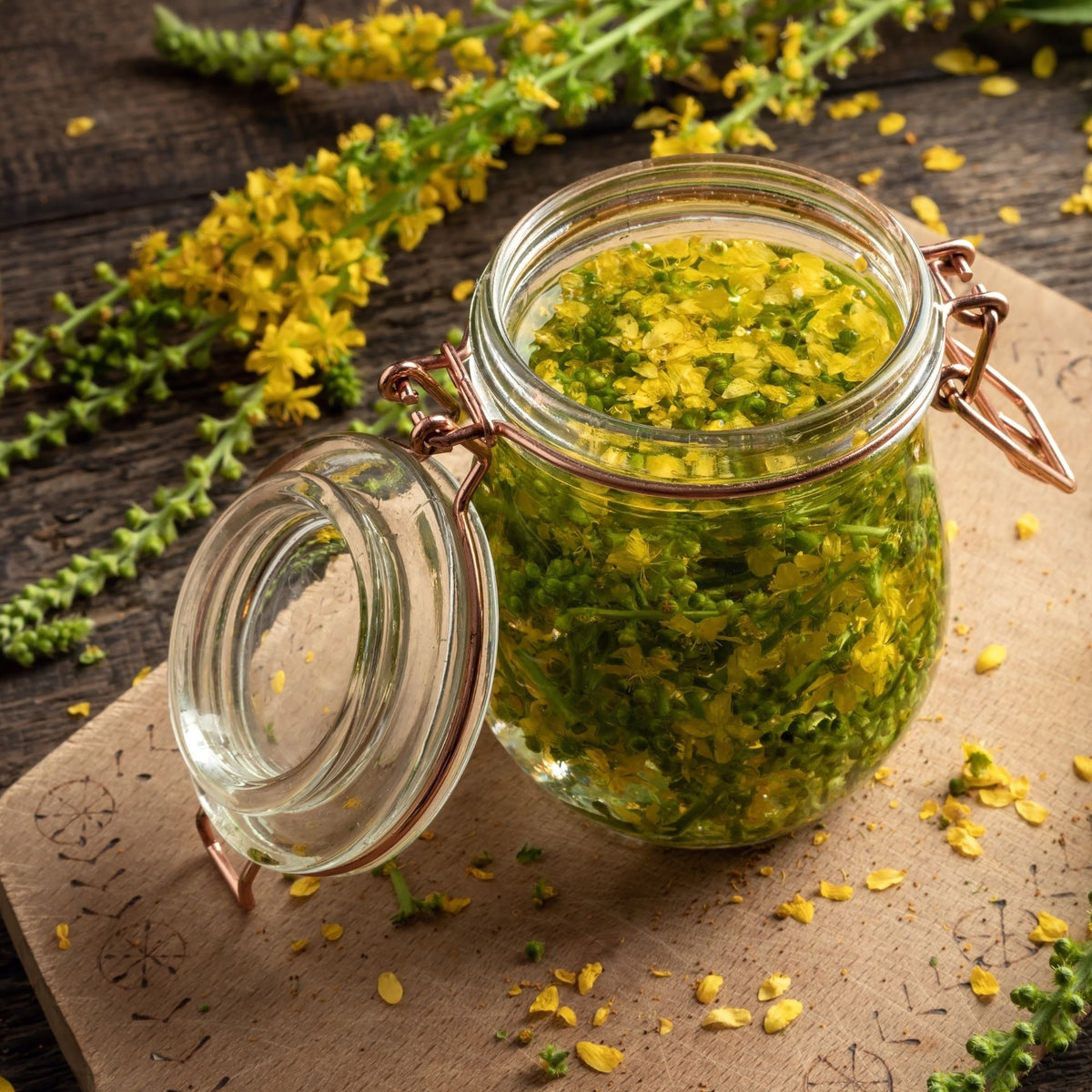 A glass jar of herbs steeping beside fresh yellow flowers